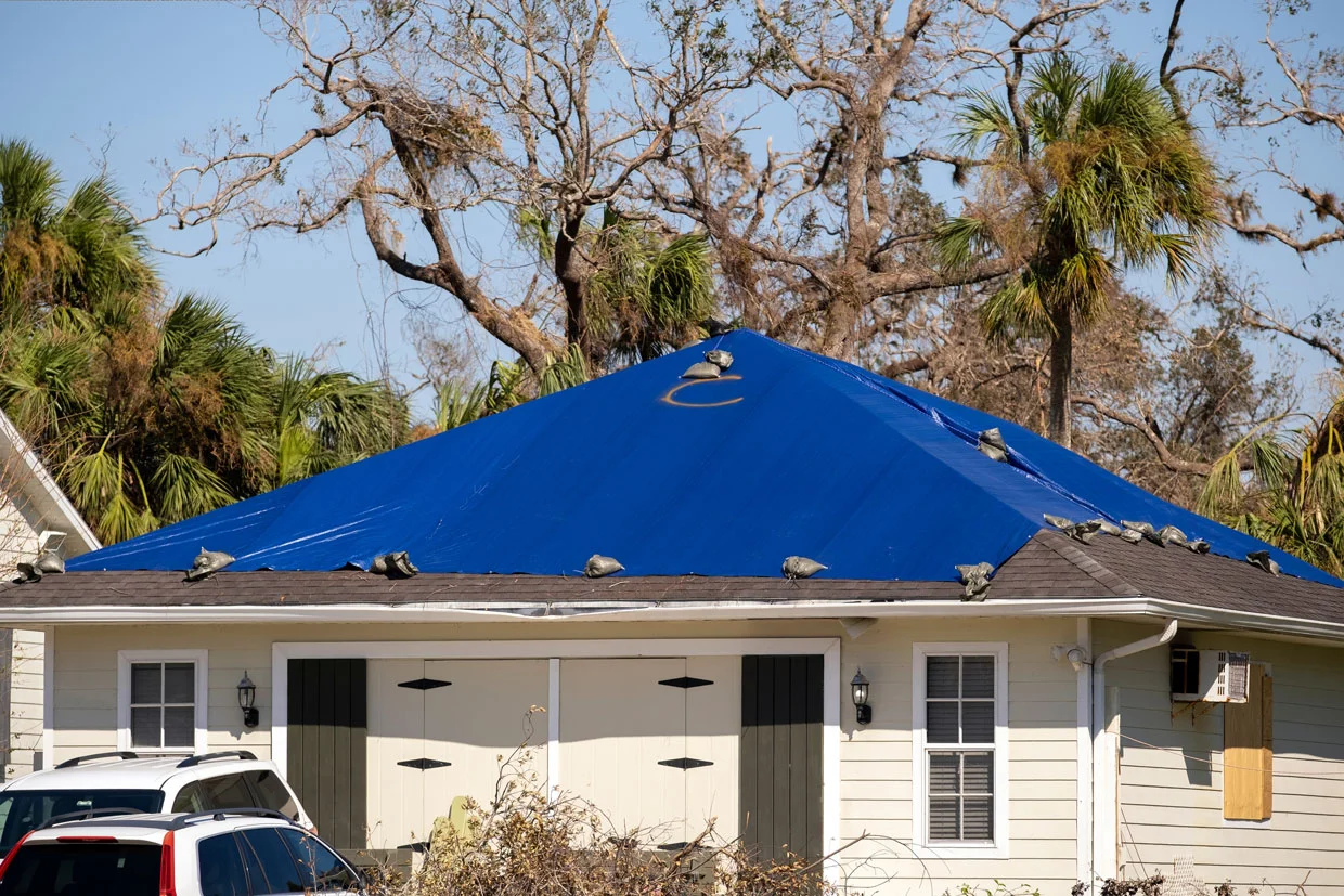 Hurricane Ian damaged the roof of the house covered with a plastic tarp to protect against rainwater leaks until the asphalt shingles were replaced. Aftermath of natural disasters